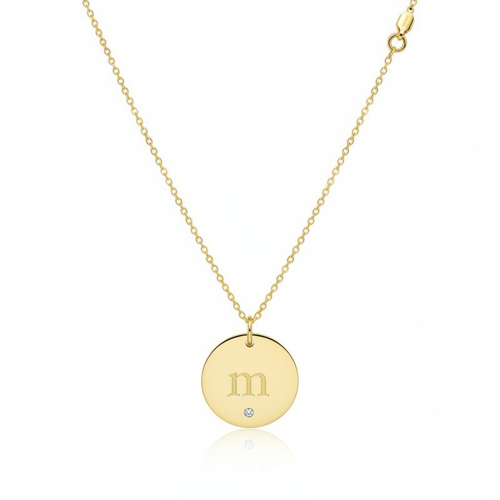 Gold necklace with a round pendant engraved with 'm' and a diamond on a white background